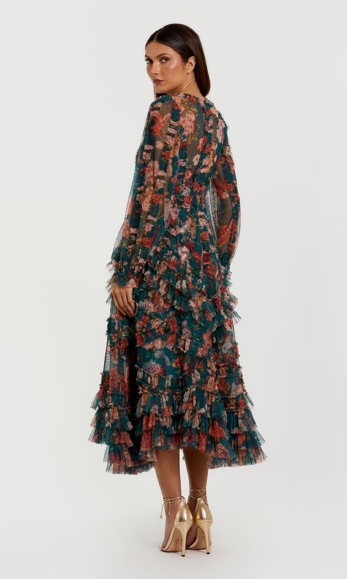 Woman wearing the Mac Duggal 8348 Floral Wedding Guest Dress with long sleeves, A-line skirt, and ruffled tiers, looking over her shoulder and paired with metallic high-heeled shoes.